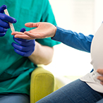 A pregnant women offers her hand while a technician readies a needle for a blood draw.