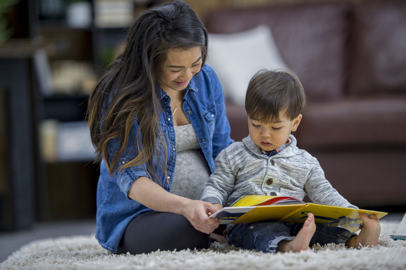 Woman and child sitting on a rug reading a book together.