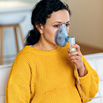Pregnant person holding an assistive breathing device to their face.