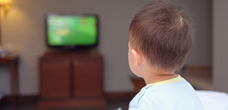 Un niño pequeño con un control remoto en la mano mirando la pantalla de un televisor.