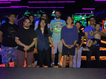Lab members pose at an indoor mini-golf course lit with neon lights and blacklights.