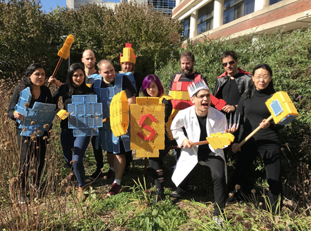 Lab members pose outside wearing 'armor' and wielding 'weapons' made of pipette tip racks.