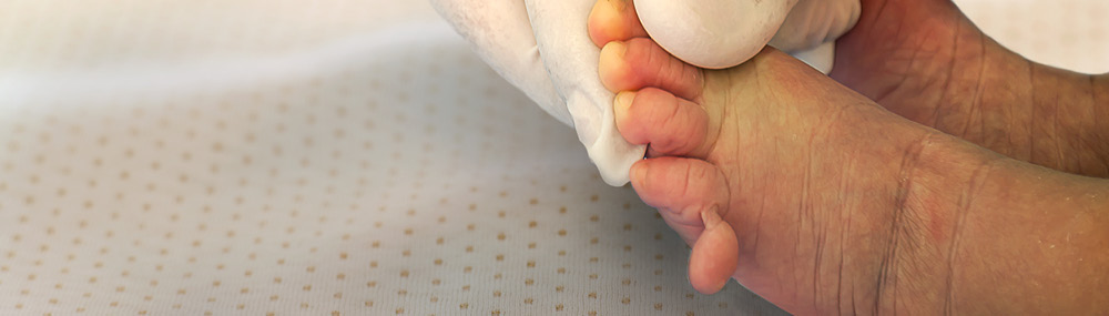 A hand wearing a rubber glove holds a newborn baby’s foot. 