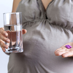 Pregnant woman holding a glass of water in one hand and vitamin pills in the other hand.