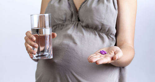 Pregnant woman holding a glass of water in one hand and vitamin pills in the other hand.