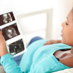 Pregnant woman sitting on the couch in the living room and looking at her ultrasound scan of the fetus.