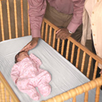 Two parents standing over a crib, with their child sleeping on its back