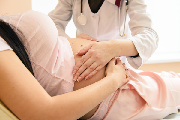 physician’s hands on a pregnant woman’s abdomen