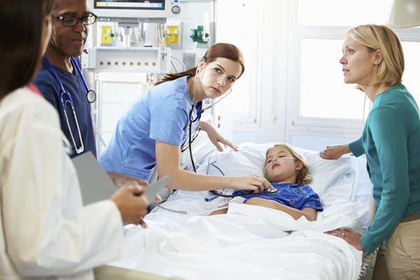 critically ill child surrounded by hospital staff Hospital staff attend to a child in bed in the pediatric critical care ward, while the child’s mother stands by the bed