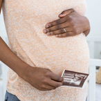 Pregnant woman’s midsection, with one hand on the top of her “bump” and the other holding a sonogram image