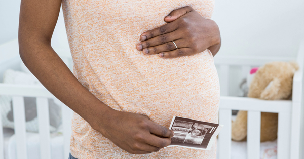 Stock photo of a pregnant woman’s midsection and hand holding ultrasound printout.