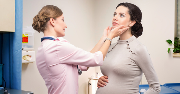 Health care provider feels the neck of a pregnant woman to check her thyroid gland