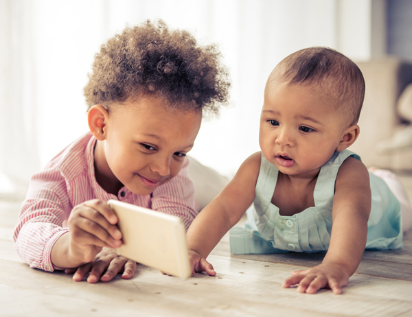 Older child showing a mobile device to a young toddler