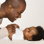 A dad smiling at a baby who is lying on her back