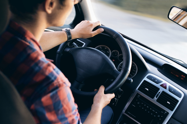 Young man in front of steering wheel, driving a car