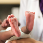 Healthcare provider in white coat holding newborn, showing baby’s feet.