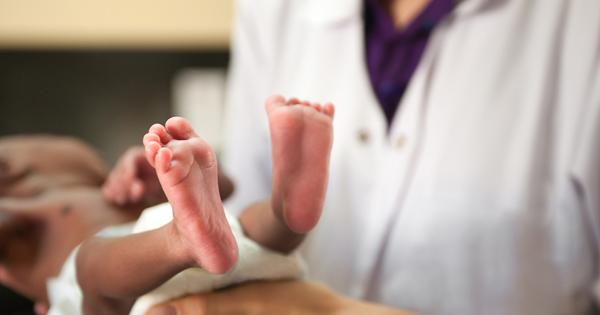 Healthcare provider in white coat holding newborn, showing baby’s feet.