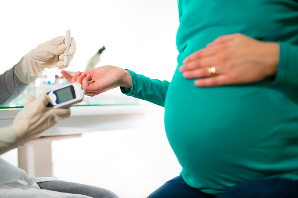 Pregnant woman offering her finger to healthcare provider for a blood test.