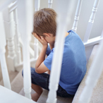 Boy with hands over face sitting on stairs