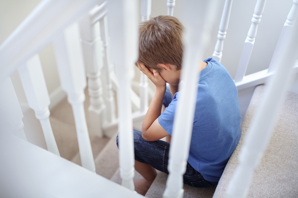 Boy with hands over face sitting on stairs