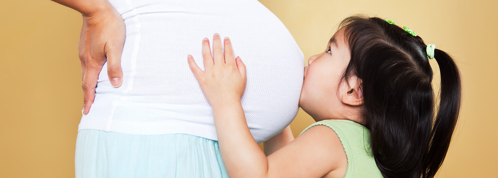 Stock image of a young girl kissing her pregnant mother’s stomach.