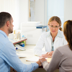 A couple sitting together and holding hands while facing a healthcare provider seated behind her desk.