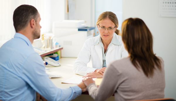 A couple sitting together and holding hands while facing a healthcare provider seated behind her desk.