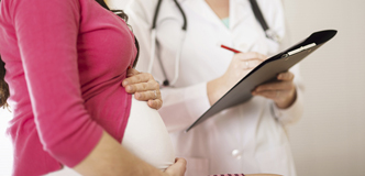 A pregnant woman stands next to a doctor filling out a form.