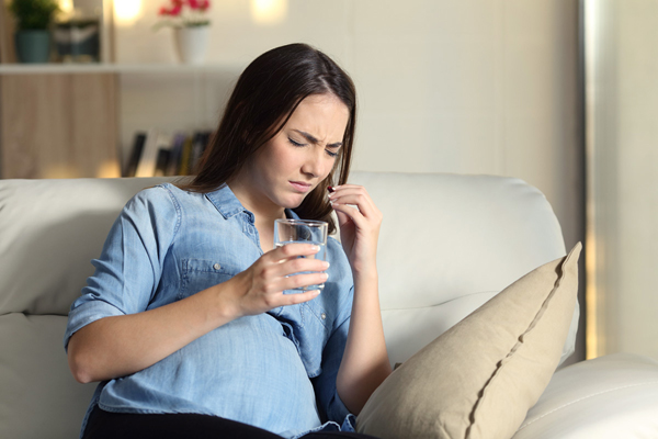 Pregnant woman with a distressed expression taking a pill.