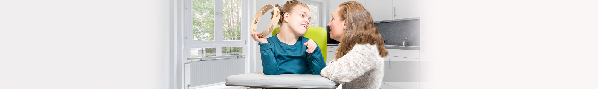 Girl with a disability holding a tambourine while her mother smiles at her.