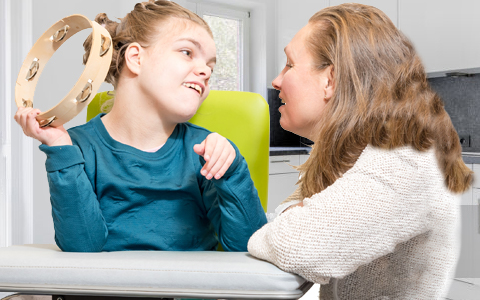 Girl with a disability holding a tambourine while her mother smiles at her.