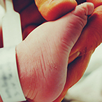 Hand grasping a newborn’s foot, which has a hospital ID tag wrapped around it.
