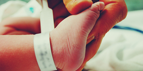 Hand grasping a newborn’s foot, which has a hospital ID tag wrapped around it.