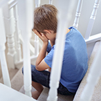 A boy seated on stairs, face resting in hands as if crying.