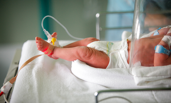 Infant in a hospital crib, feet and torso visible, with medical devices attached to feet.