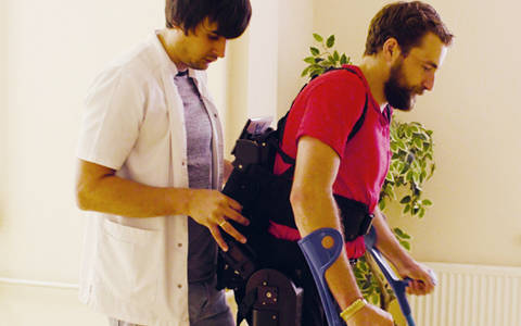 A male nurse helping a young man with a disability walk in a robotic skeleton.