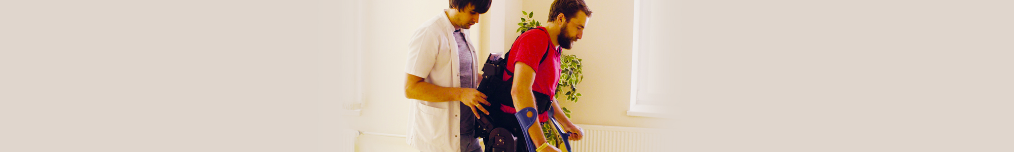 A male nurse helping a young man with a disability walk in a robotic skeleton.