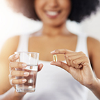 Smiling woman holding a glass of water and a pill-sized capsule.