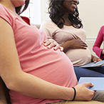 Pregnant woman in forefront of group of women holding her belly.