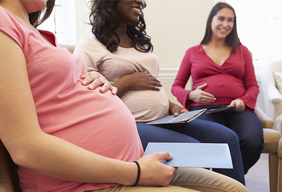 Pregnant woman in forefront of group of women holding her belly.