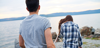 Stock image of a young couple on the shore of a river or a lake, the woman appears to be walking away from the man.