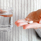 A close up of a person’s hands holding a glass of water and a pill.