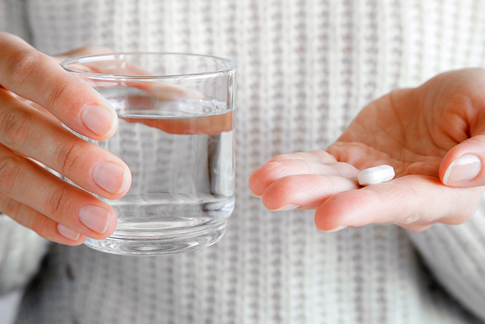 A close up of a person’s hands holding a glass of water and a pill.