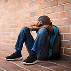 Child seated, leaning against brick wall, face resting on crossed arms.