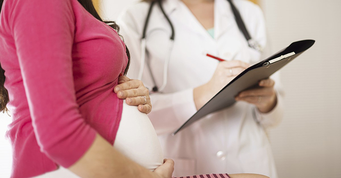 Pregnant woman and her healthcare provider, with a focus on the woman’s belly and the provider’s clipboard. 