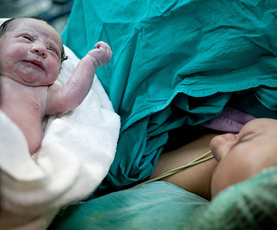 Mother who just gave birth being handed her newborn baby wrapped in a blanket.
