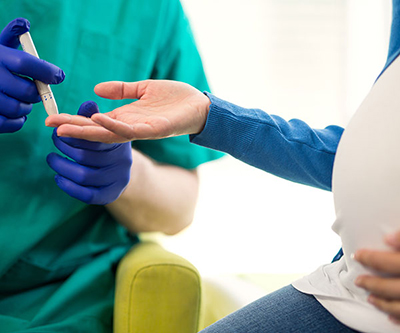 Medical professional’s hands using a glucometer on the finger of a pregnant woman.