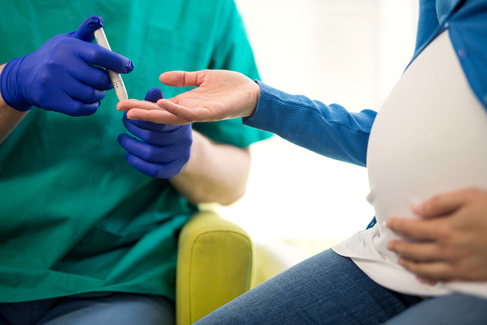 A pregnant women offers her hand while a technician readies a needle for a blood draw.