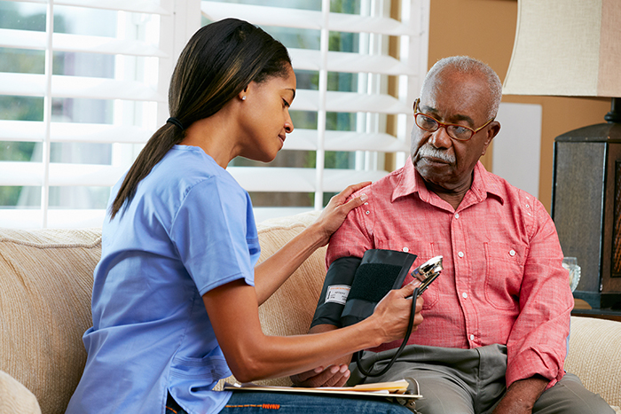 A nurse takes the blood pressure of an elderly man. Both are African-American.