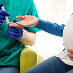 Pregnant woman offering her finger to a technician for a finger stick blood sample.